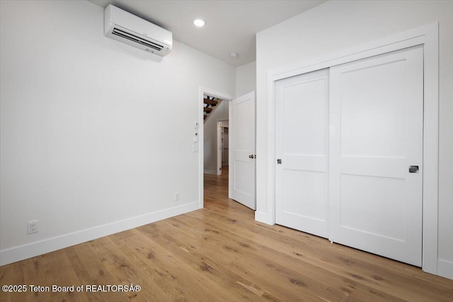 unfurnished bedroom featuring a closet, a wall mounted air conditioner, and light hardwood / wood-style flooring