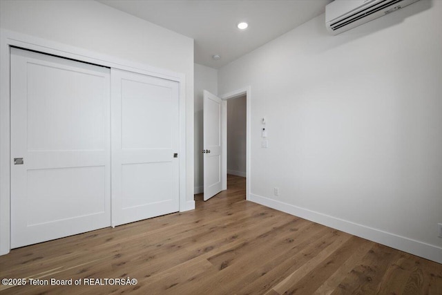 unfurnished bedroom with hardwood / wood-style flooring, a wall mounted air conditioner, and a closet