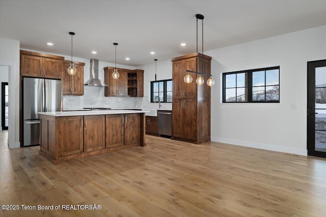 kitchen with a center island, wall chimney range hood, hanging light fixtures, and appliances with stainless steel finishes