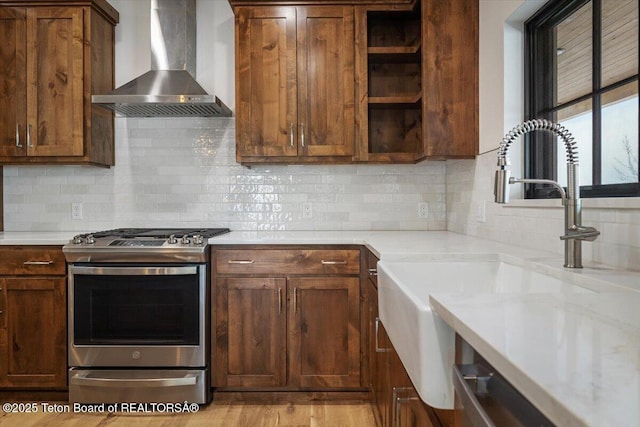 kitchen with stainless steel gas range, sink, tasteful backsplash, light stone countertops, and wall chimney range hood