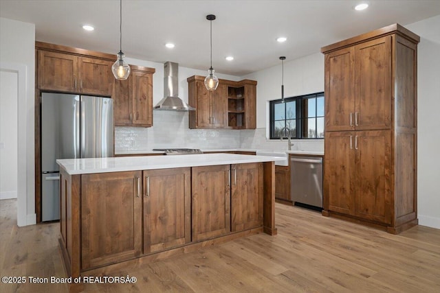 kitchen with a kitchen island, appliances with stainless steel finishes, decorative light fixtures, light hardwood / wood-style floors, and wall chimney exhaust hood