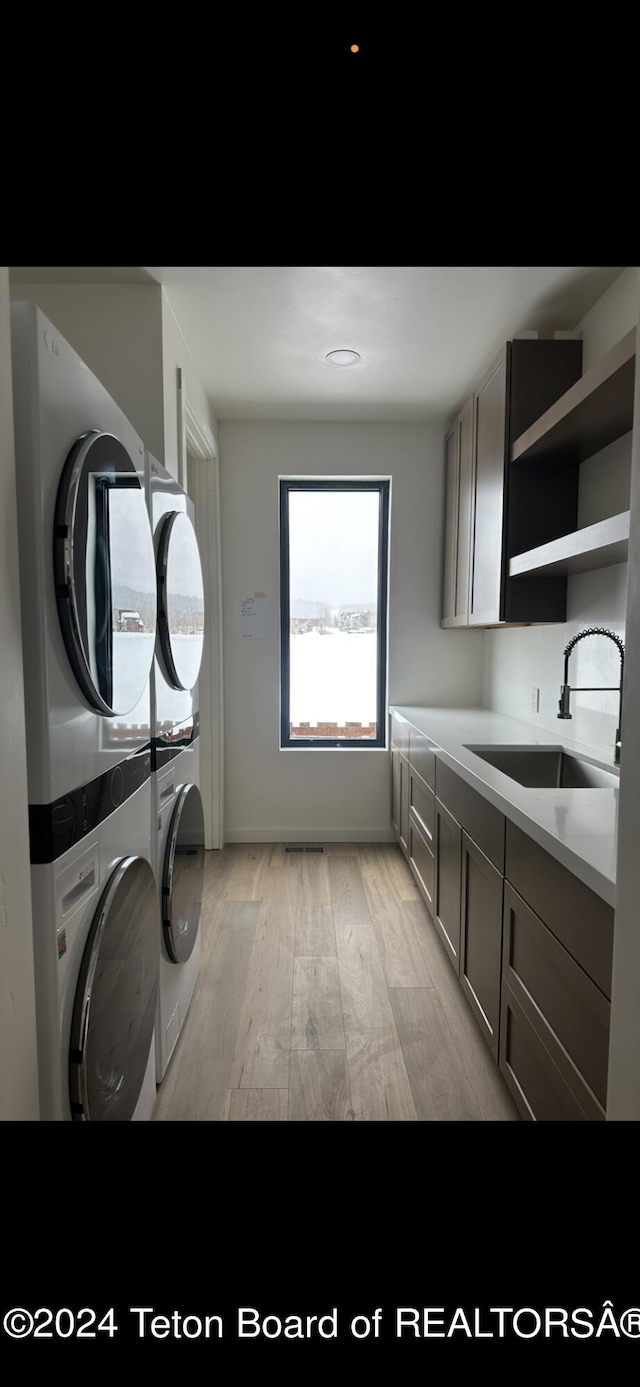 washroom featuring stacked washing maching and dryer, cabinets, sink, and light wood-type flooring