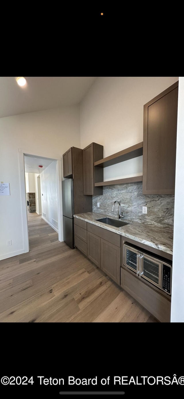 kitchen with vaulted ceiling, sink, stainless steel fridge, wood-type flooring, and tasteful backsplash