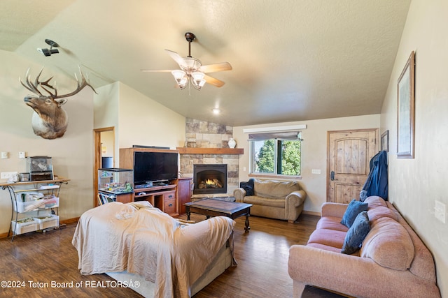 living room with ceiling fan, a stone fireplace, a textured ceiling, vaulted ceiling, and dark hardwood / wood-style flooring