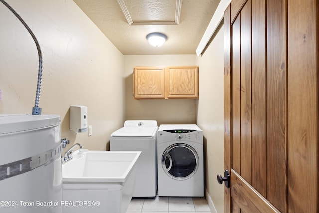 laundry room featuring water heater, light tile patterned flooring, a textured ceiling, cabinets, and washer and dryer