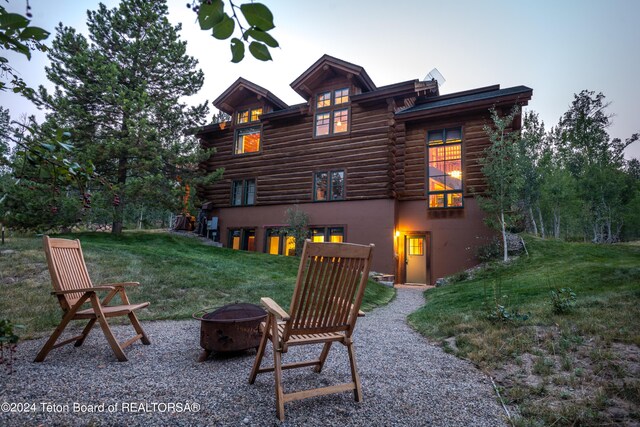 rear view of house with stucco siding, log siding, a yard, and an outdoor fire pit