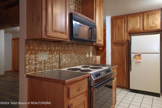 kitchen featuring electric range, white refrigerator, decorative backsplash, and light tile patterned flooring