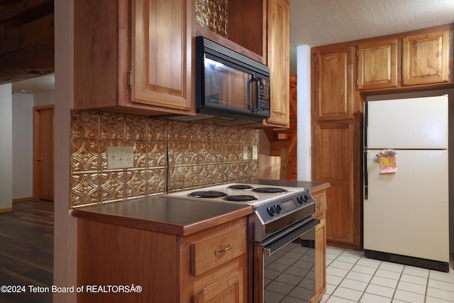 kitchen featuring tasteful backsplash, black microwave, light tile patterned floors, freestanding refrigerator, and electric range