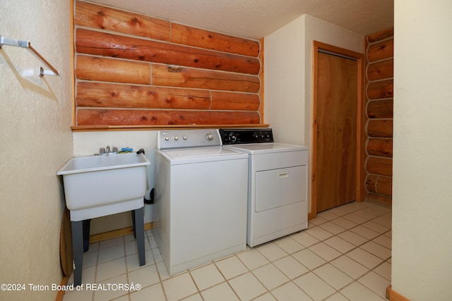 laundry area with light tile patterned floors, a textured ceiling, washer and dryer, and sink