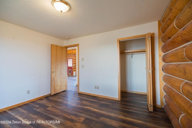 unfurnished bedroom with rustic walls, baseboards, a textured ceiling, and dark wood finished floors