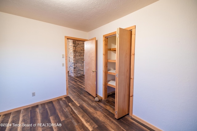 unfurnished bedroom with dark wood-style floors, a textured ceiling, and baseboards