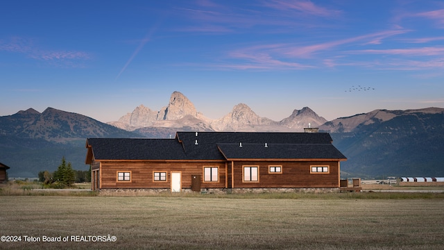 back house at dusk with a mountain view and a yard