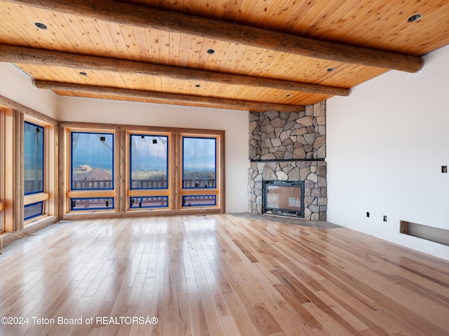 unfurnished living room with a stone fireplace, light hardwood / wood-style floors, wooden ceiling, beam ceiling, and a healthy amount of sunlight