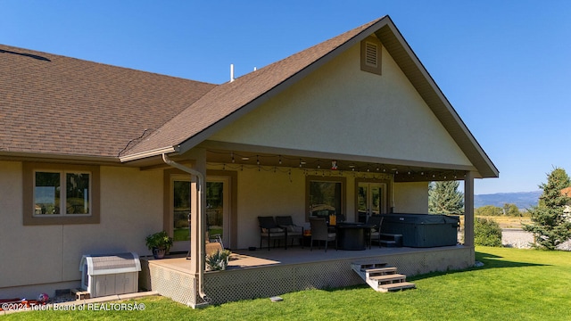 rear view of property featuring a hot tub, a lawn, and a patio