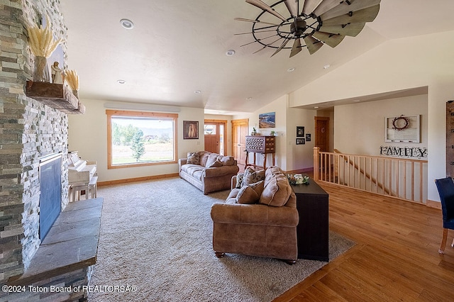 living room with lofted ceiling, ceiling fan, hardwood / wood-style floors, and a stone fireplace