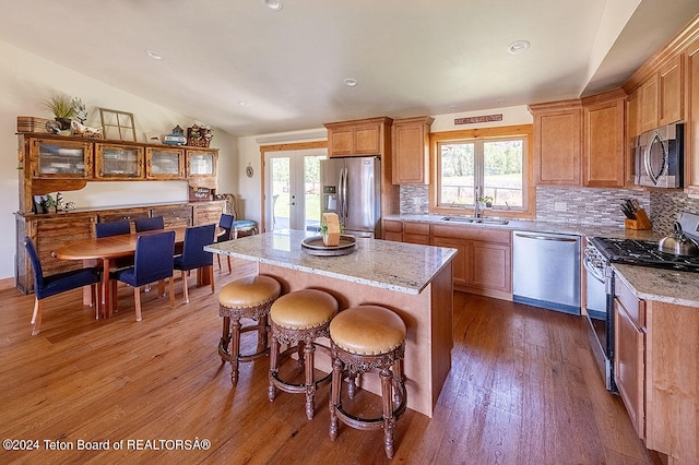 kitchen featuring hardwood / wood-style flooring, light stone counters, stainless steel appliances, sink, and a kitchen island