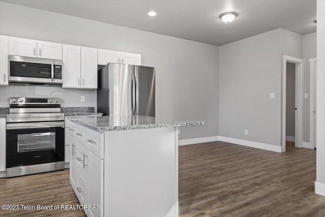 kitchen with appliances with stainless steel finishes, light stone counters, white cabinets, a kitchen island, and dark hardwood / wood-style flooring