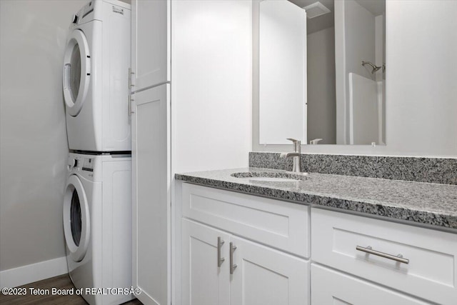 clothes washing area with stacked washer and clothes dryer, sink, dark hardwood / wood-style flooring, and cabinets