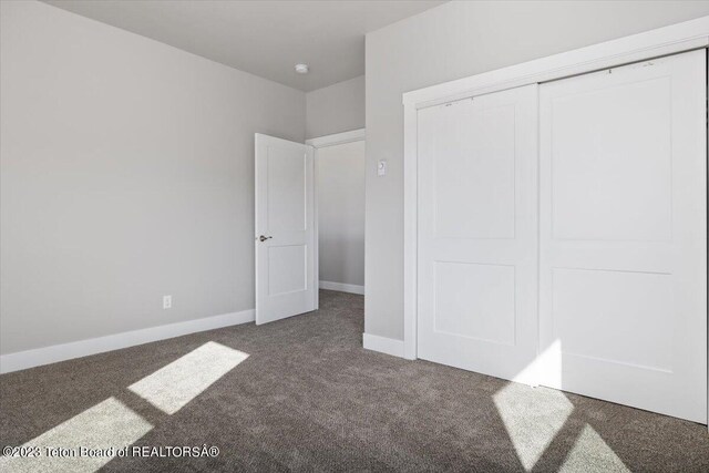 unfurnished bedroom with dark colored carpet and a closet