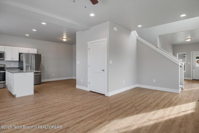 kitchen with a kitchen island, white cabinetry, light stone counters, stainless steel appliances, and light hardwood / wood-style flooring