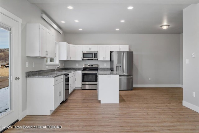 kitchen featuring sink, white cabinetry, dark stone countertops, stainless steel appliances, and a center island