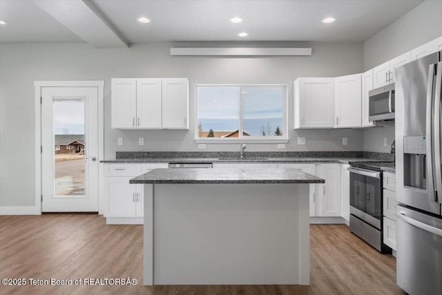 kitchen with a kitchen island, white cabinetry, sink, dark stone countertops, and stainless steel appliances