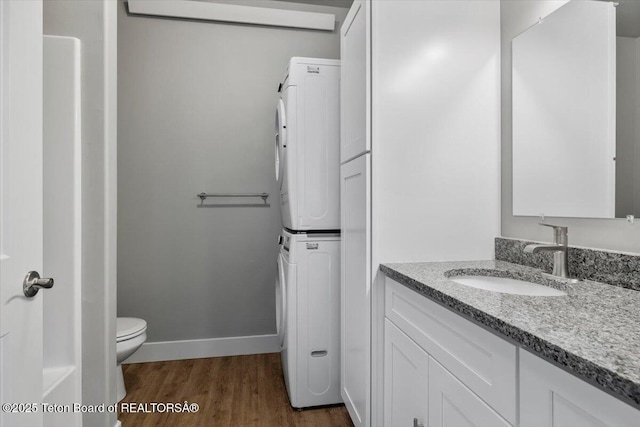 bathroom with stacked washer / dryer, toilet, hardwood / wood-style floors, and vanity