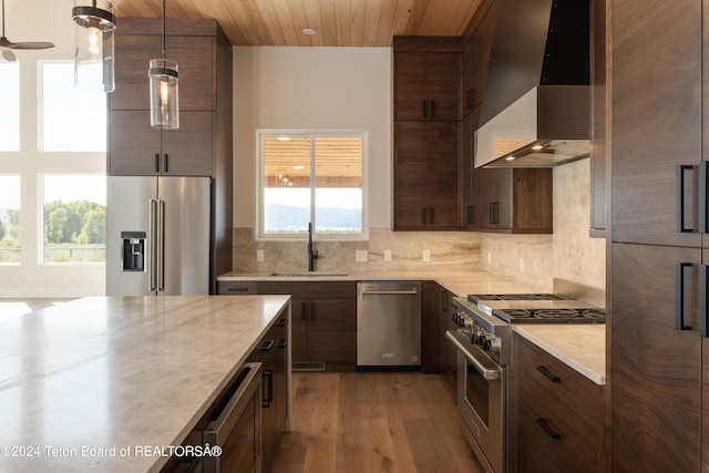 kitchen with plenty of natural light, dark wood-type flooring, high end appliances, hanging light fixtures, and wall chimney range hood