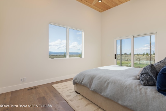 bedroom with a towering ceiling, multiple windows, hardwood / wood-style flooring, and wooden ceiling