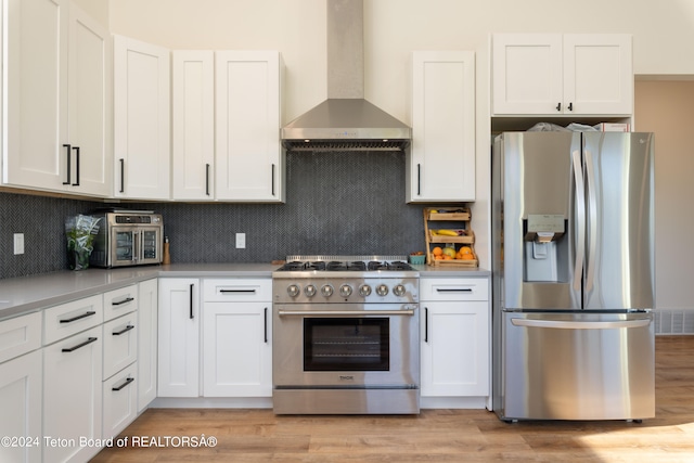 kitchen featuring light hardwood / wood-style flooring, stainless steel appliances, white cabinetry, and wall chimney range hood