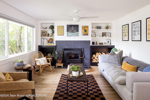 living room with hardwood / wood-style floors, built in shelves, a wood stove, and ceiling fan