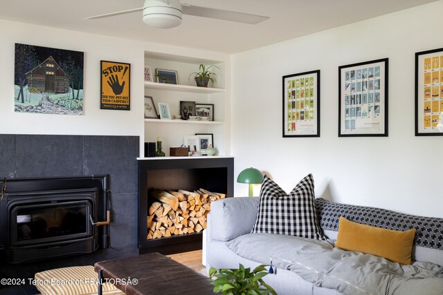 living room with ceiling fan, hardwood / wood-style flooring, a wood stove, and built in shelves