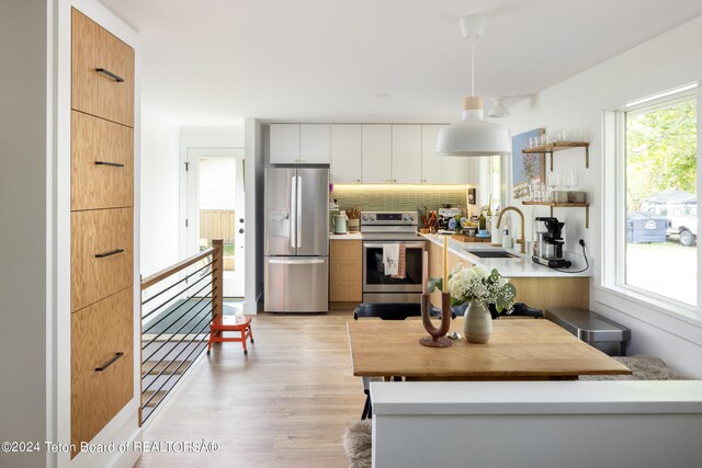 kitchen featuring a healthy amount of sunlight, sink, white cabinetry, stainless steel appliances, and pendant lighting