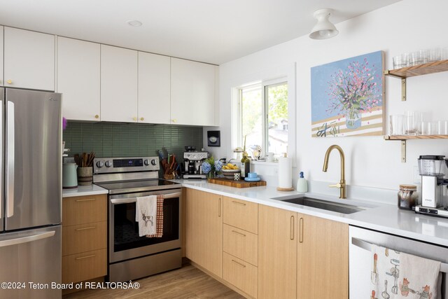 kitchen featuring light brown cabinets, white cabinetry, sink, light hardwood / wood-style floors, and stainless steel appliances