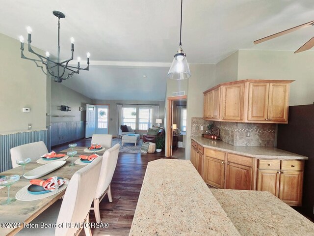 kitchen featuring light stone counters, tasteful backsplash, ceiling fan with notable chandelier, hanging light fixtures, and dark hardwood / wood-style flooring