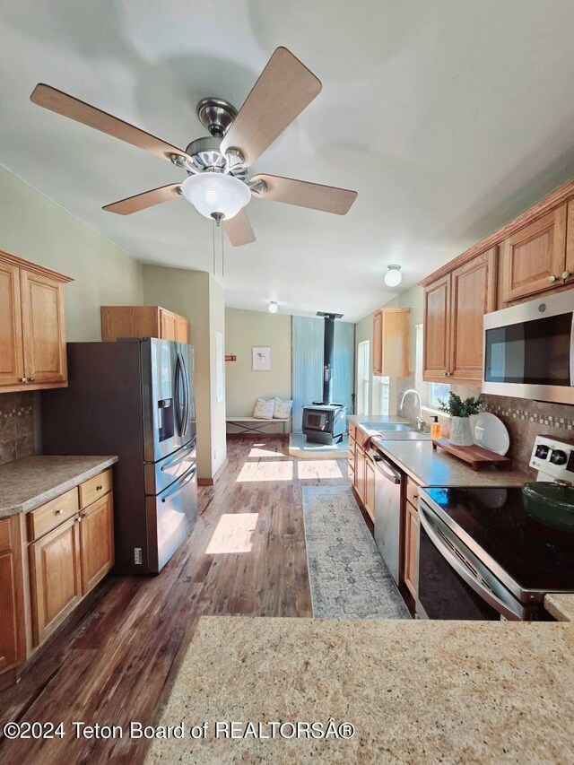 kitchen featuring dark hardwood / wood-style floors, a wood stove, decorative backsplash, appliances with stainless steel finishes, and ceiling fan