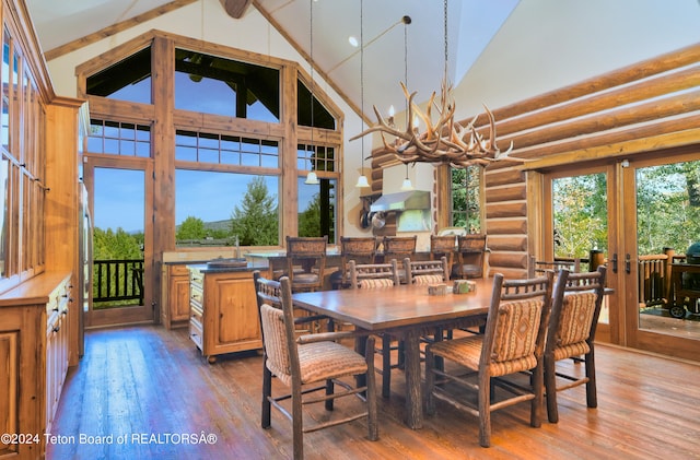 dining room featuring hardwood / wood-style flooring, sink, a notable chandelier, high vaulted ceiling, and rustic walls