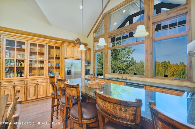 kitchen featuring high vaulted ceiling, pendant lighting, stainless steel appliances, light wood-type flooring, and sink