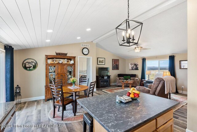 kitchen featuring ceiling fan with notable chandelier, pendant lighting, lofted ceiling with beams, dark hardwood / wood-style floors, and a kitchen island