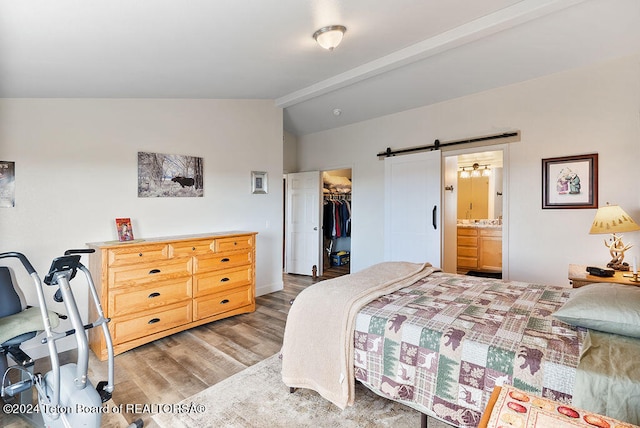 bedroom featuring a walk in closet, a barn door, connected bathroom, light hardwood / wood-style floors, and a closet