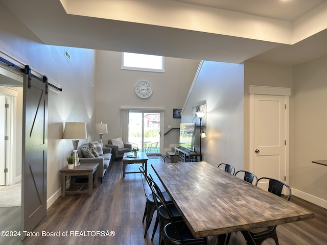 dining area with a towering ceiling, a barn door, and dark hardwood / wood-style flooring