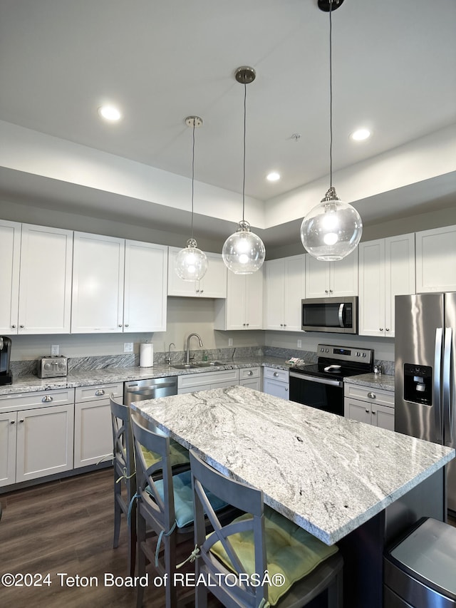 kitchen with pendant lighting, dark wood-type flooring, white cabinetry, appliances with stainless steel finishes, and light stone countertops