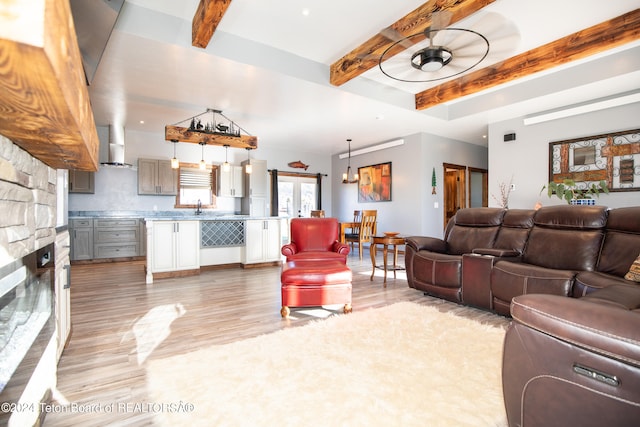 living room with light hardwood / wood-style floors, a stone fireplace, beam ceiling, ceiling fan, and sink