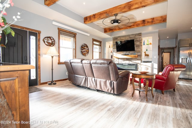 living room featuring light hardwood / wood-style floors, a fireplace, ceiling fan, and beamed ceiling