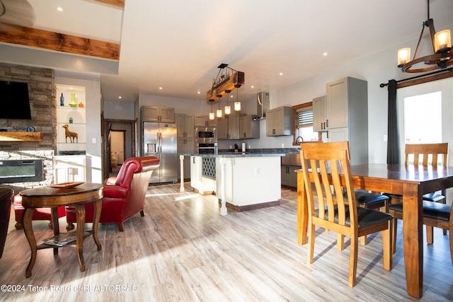 dining space with a stone fireplace, light hardwood / wood-style flooring, beam ceiling, and a wealth of natural light