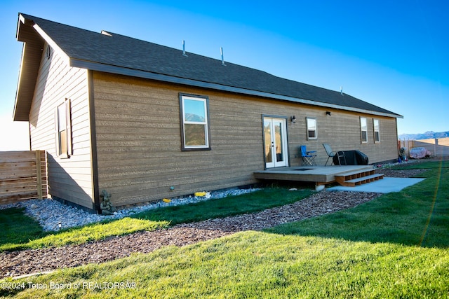 rear view of house with a lawn, a wooden deck, and french doors