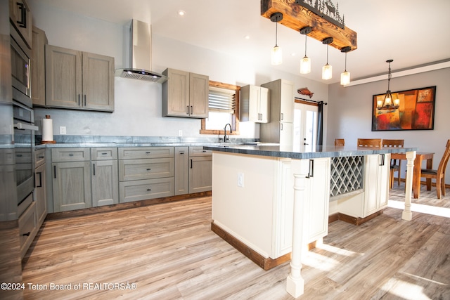 kitchen with a kitchen breakfast bar, light hardwood / wood-style flooring, hanging light fixtures, and wall chimney range hood