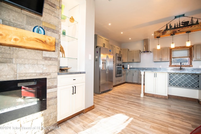 kitchen with pendant lighting, a stone fireplace, wall chimney exhaust hood, light hardwood / wood-style flooring, and stainless steel appliances