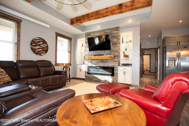 living room featuring light wood-type flooring, a stone fireplace, and beam ceiling