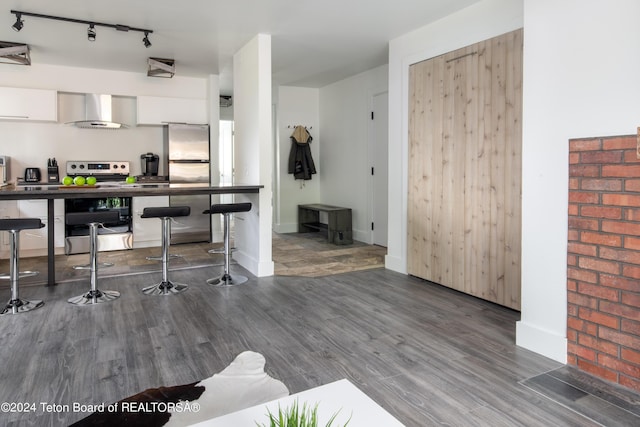kitchen with track lighting, appliances with stainless steel finishes, wall chimney exhaust hood, and wood finished floors